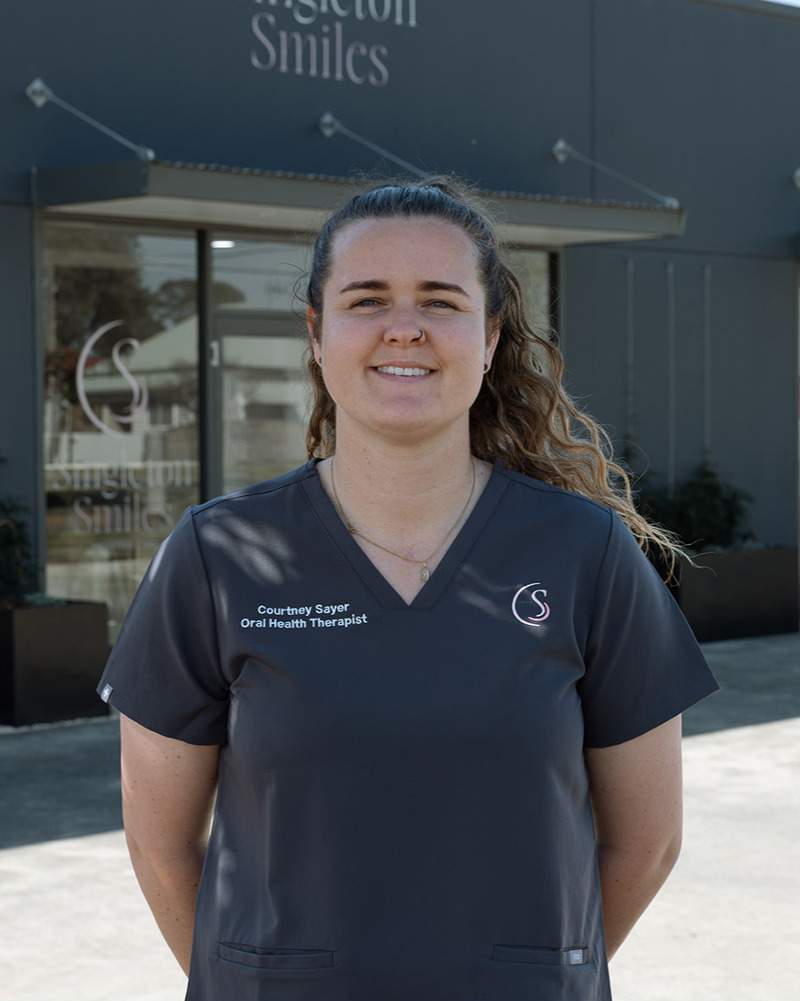 Courtney, Oral Health Therapist at Singleton Smiles, smiling outdoors in black scrubs uniform