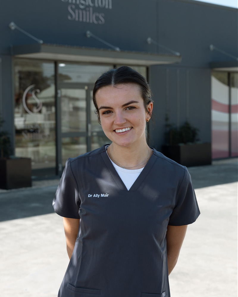 Dr Ally Moir, dentist at Singleton Smiles, smiling warmly in black scrubs seated in a modern dental practice waiting area