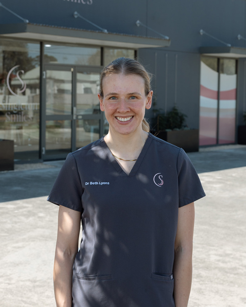 Dr Beth Lyons, dentist at Singleton Smiles, smiling warmly in dark grey scrubs inside the dental practice