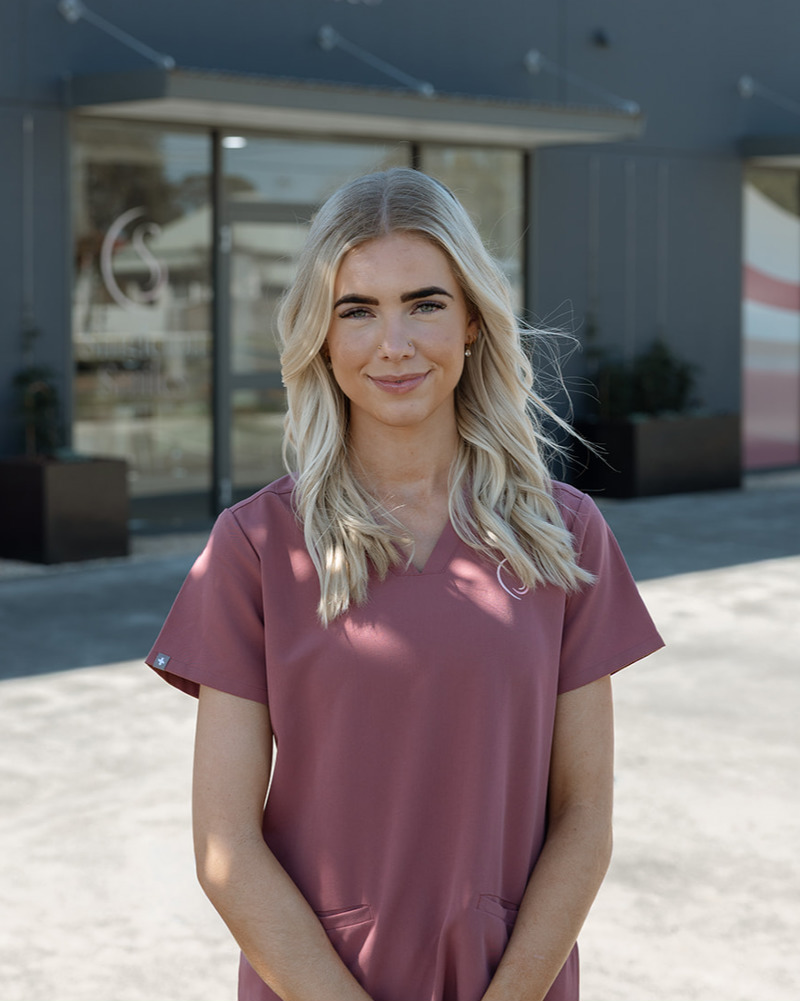 Jess, Practice Coordinator at Singleton Smiles, smiling warmly in rose scrubs in a modern dental practice setting