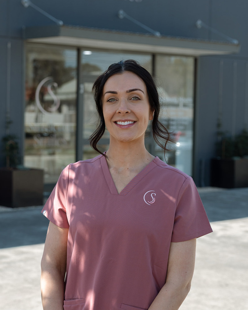 Matilda, Practice Manager at Singleton Smiles, smiling warmly in pink scrubs seated in dental practice reception area