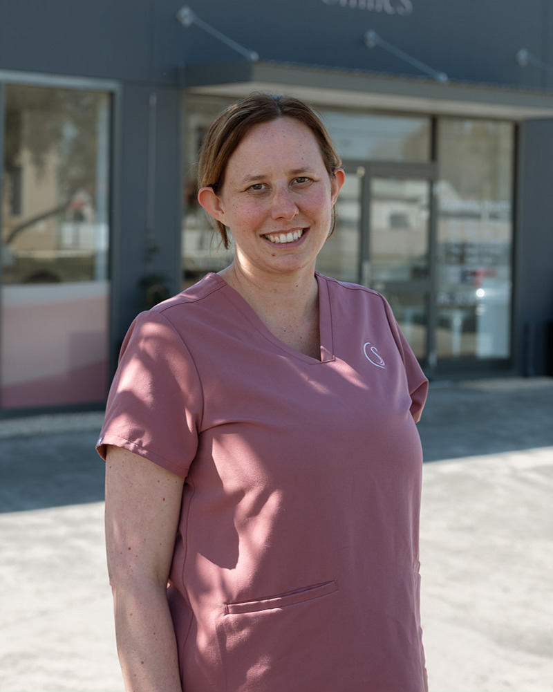 Sam, senior dental assistant, smiling warmly in pink scrubs seated in a dental practice waiting area