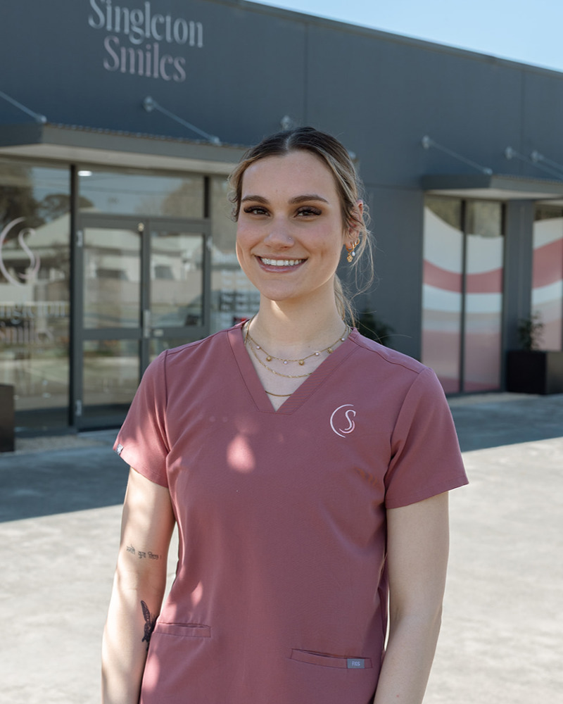 Tahlia, dental assistant at The Happy Tooth Singleton, smiling warmly in pink scrubs seated in a modern dental practice waiting area