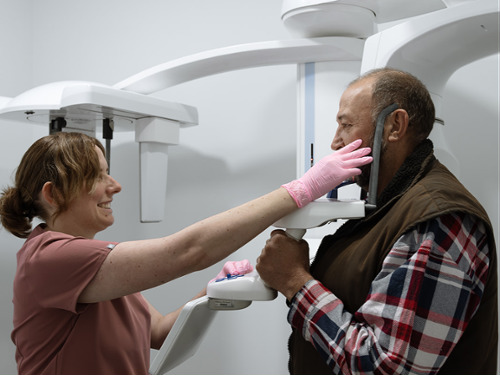 Dental team member positioning male patient for CBCT cone beam 3D imaging scan