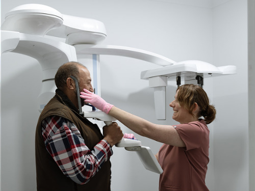 Dental assistant positioning male patient for panoramic X-ray imaging machine scan